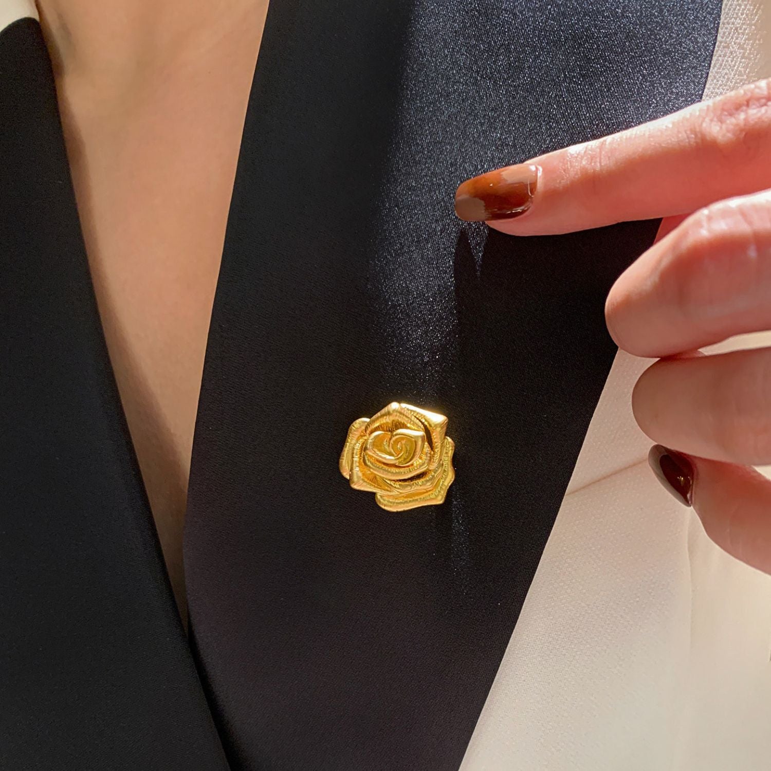 Gold rose brooch worn on a black blazer lapel with minimalist floral styling.