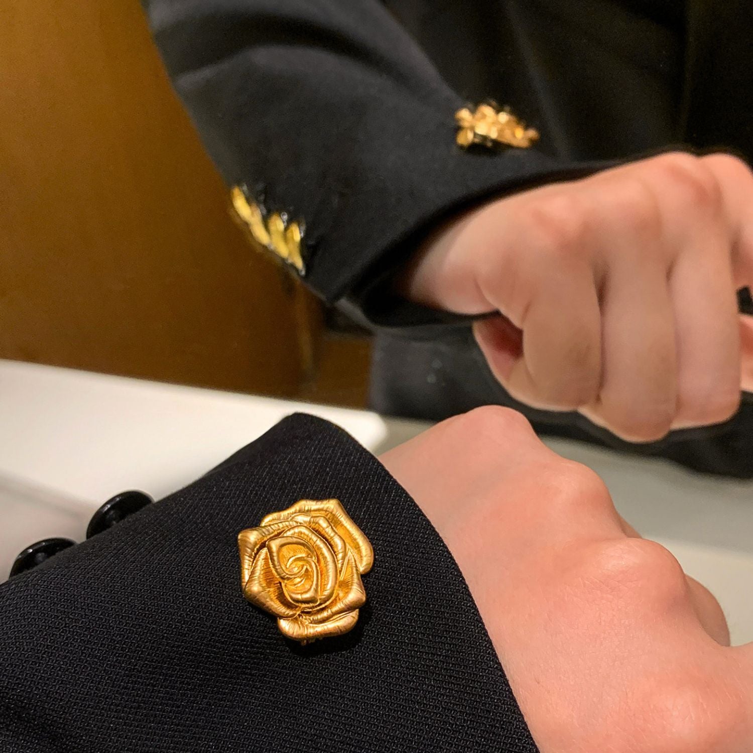 Gold rose brooch styled on a black sleeve, showing elegant cuff and lapel-inspired styling.