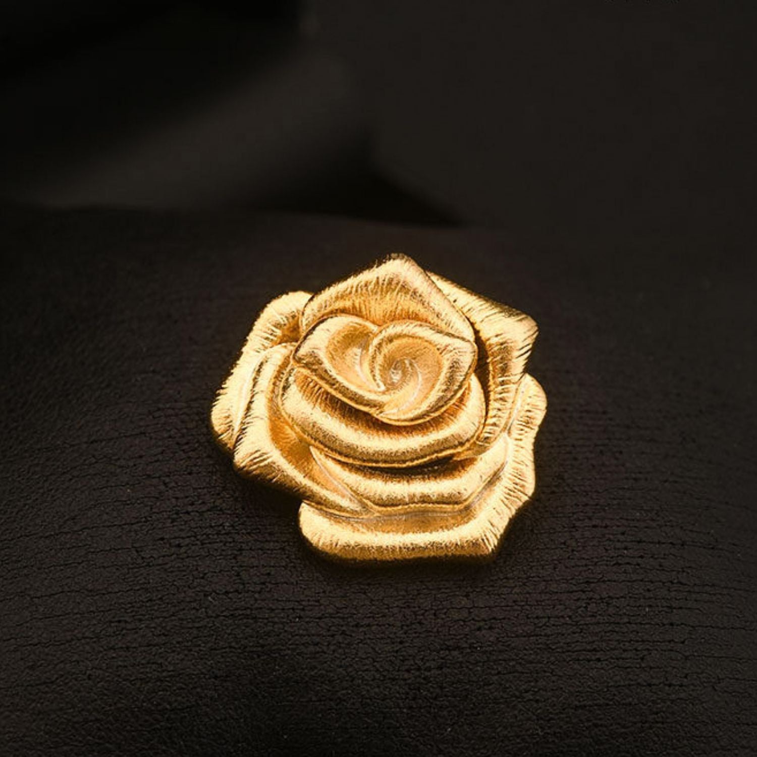 A Rose Is a Rose gold rose brooch with sculptural layered petals and etched texture on black fabric.