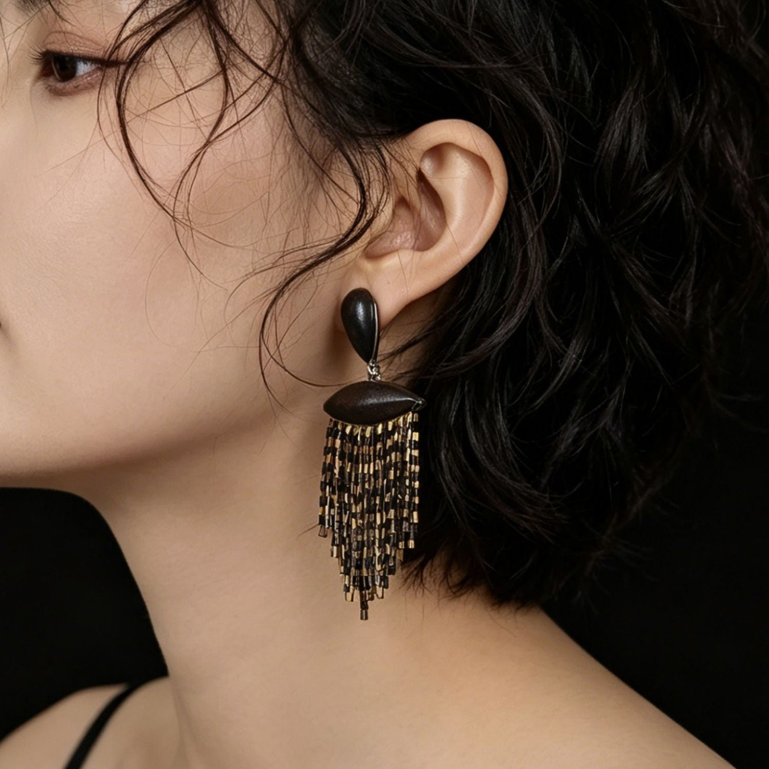 Close-up of ebony wood black and gold fringe drop earrings with layered glass seed bead tassels.