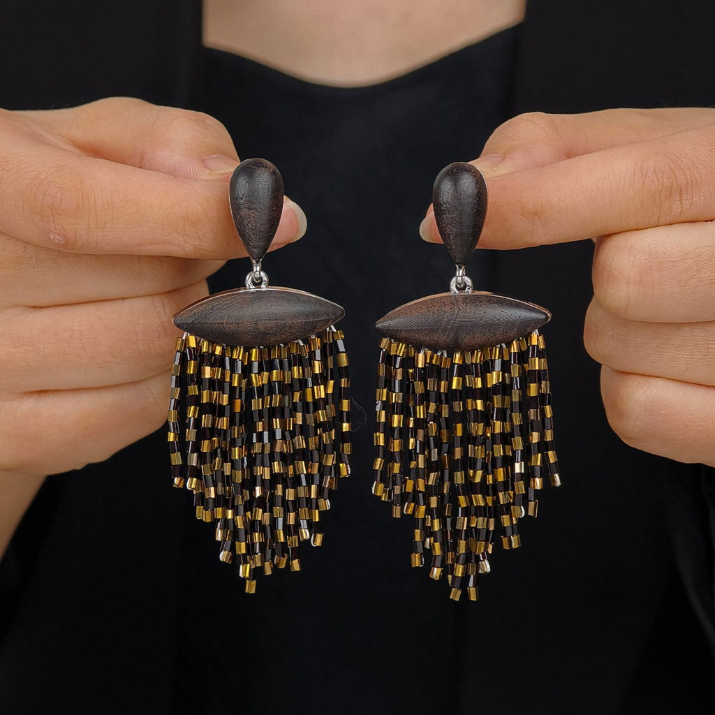 Ebony wood black and gold fringe drop earrings with hand-beaded tassel detail held against a dark background.