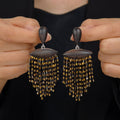 Ebony wood black and gold fringe drop earrings with hand-beaded tassel detail held against a dark background.