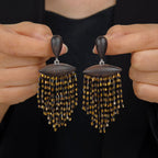 Ebony wood black and gold fringe drop earrings with hand-beaded tassel detail held against a dark background.