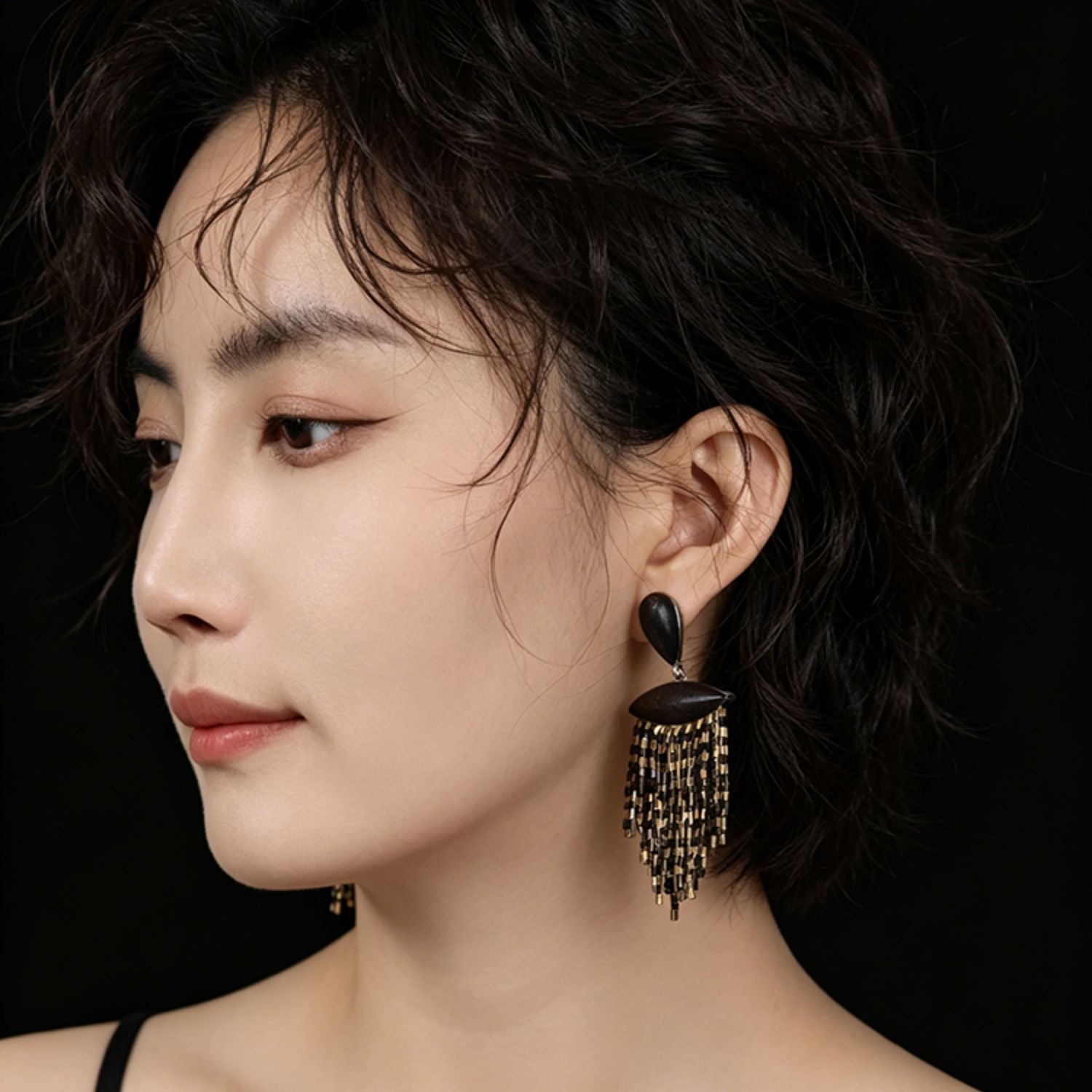 Model wearing ebony wood black and gold fringe drop earrings with cascading beaded tassels.