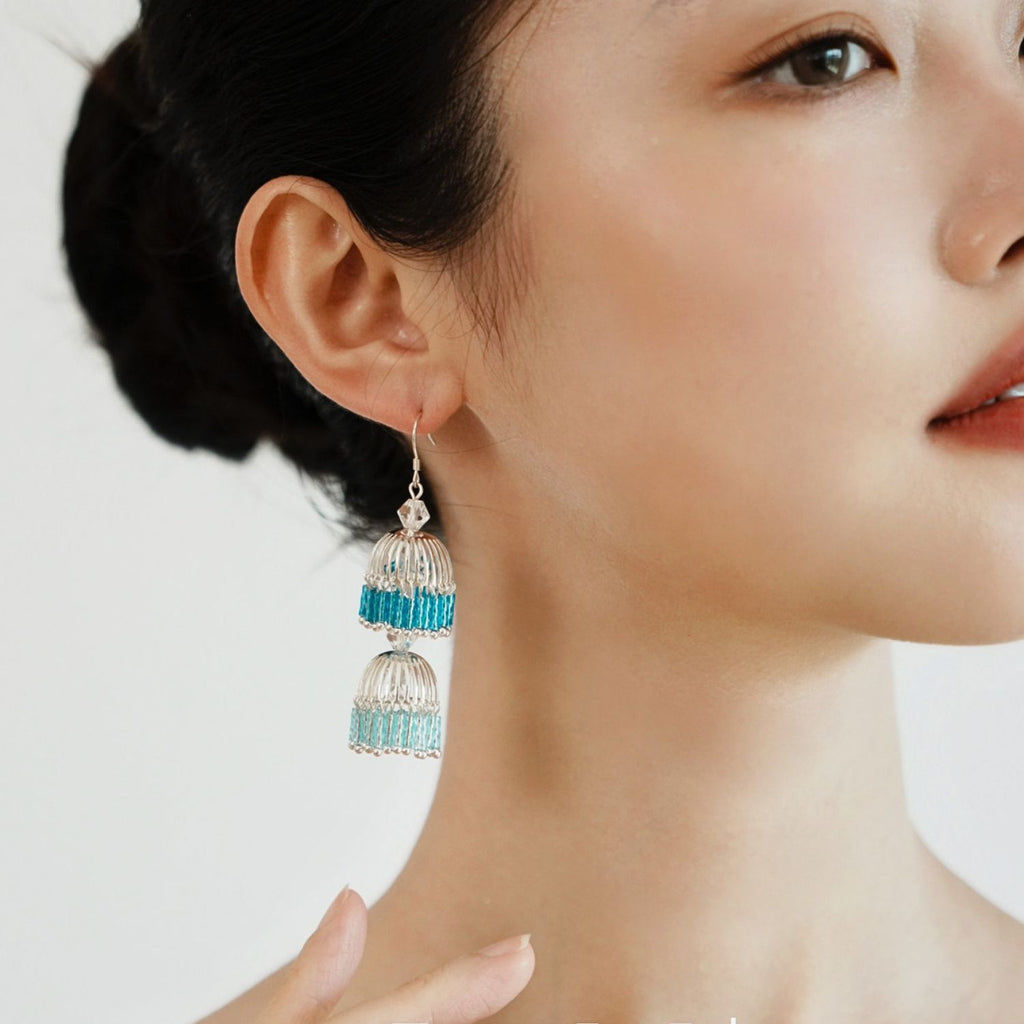 Model wearing blue gradient bugle bead lantern drop earrings with clear beadwork and soft tassel movement.