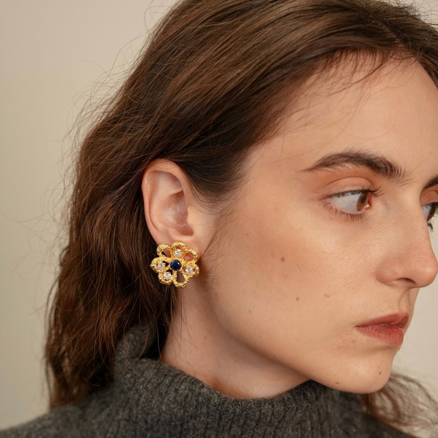 Model wearing Eternal Blossom gold flower stud earrings with openwork petals and sapphire-blue centre detail.