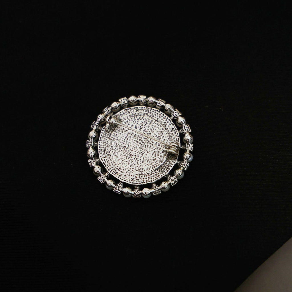 Close-up of vintage elephant brooch with faux pearl border and marbled cream-toned centre.