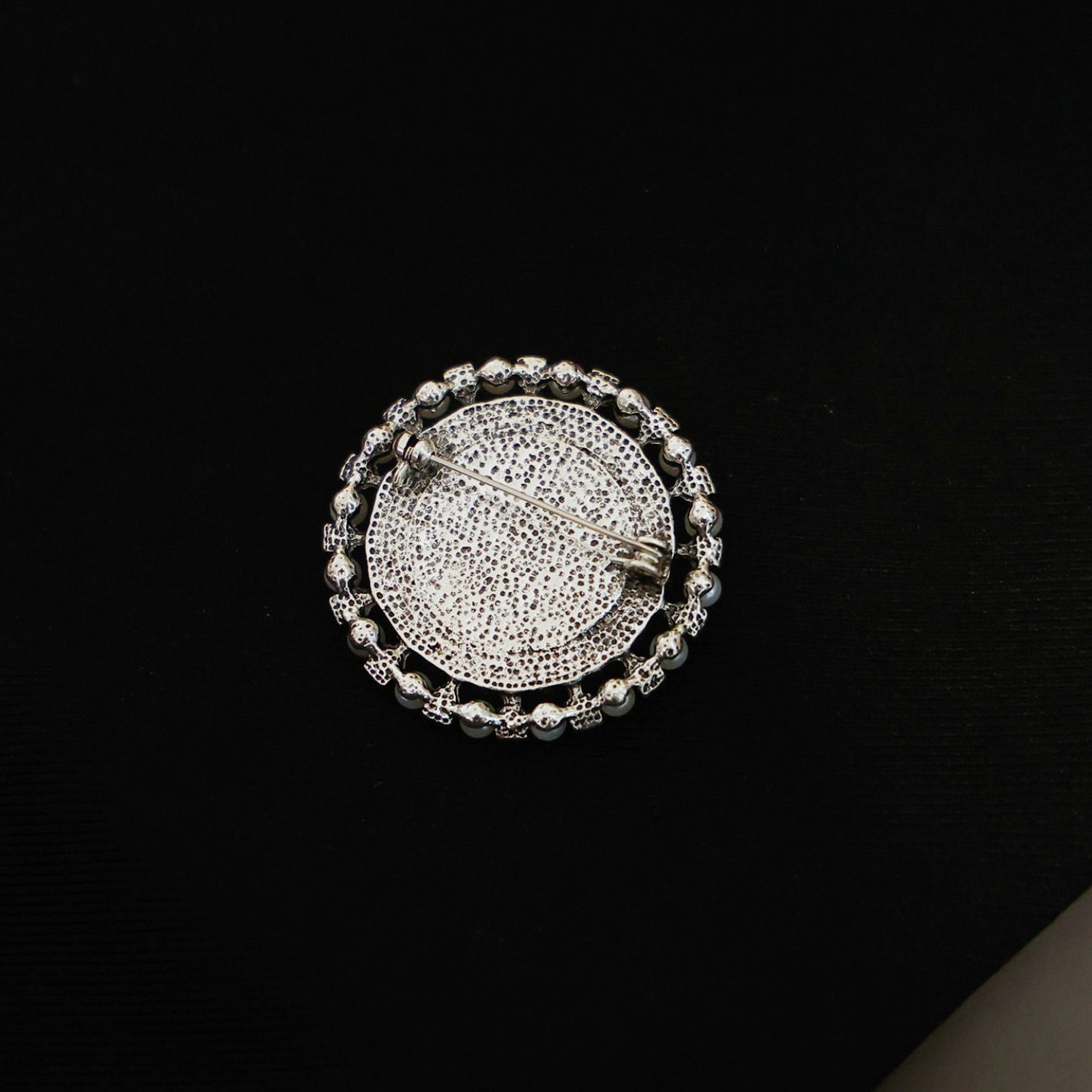 Close-up of vintage elephant brooch with faux pearl border and marbled cream-toned centre.