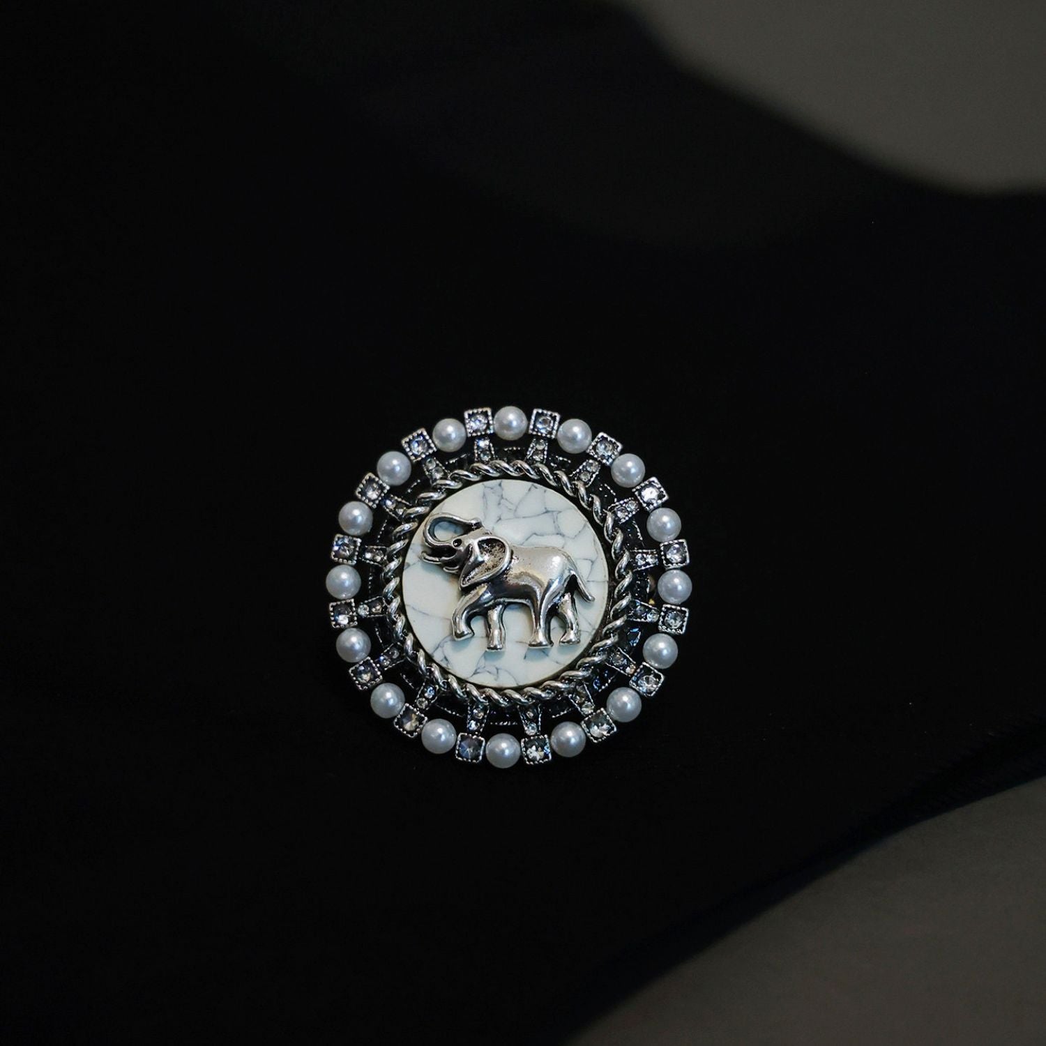 Gentle Guardian elephant brooch styled on dark fabric with silver-tone frame and pearl accents.