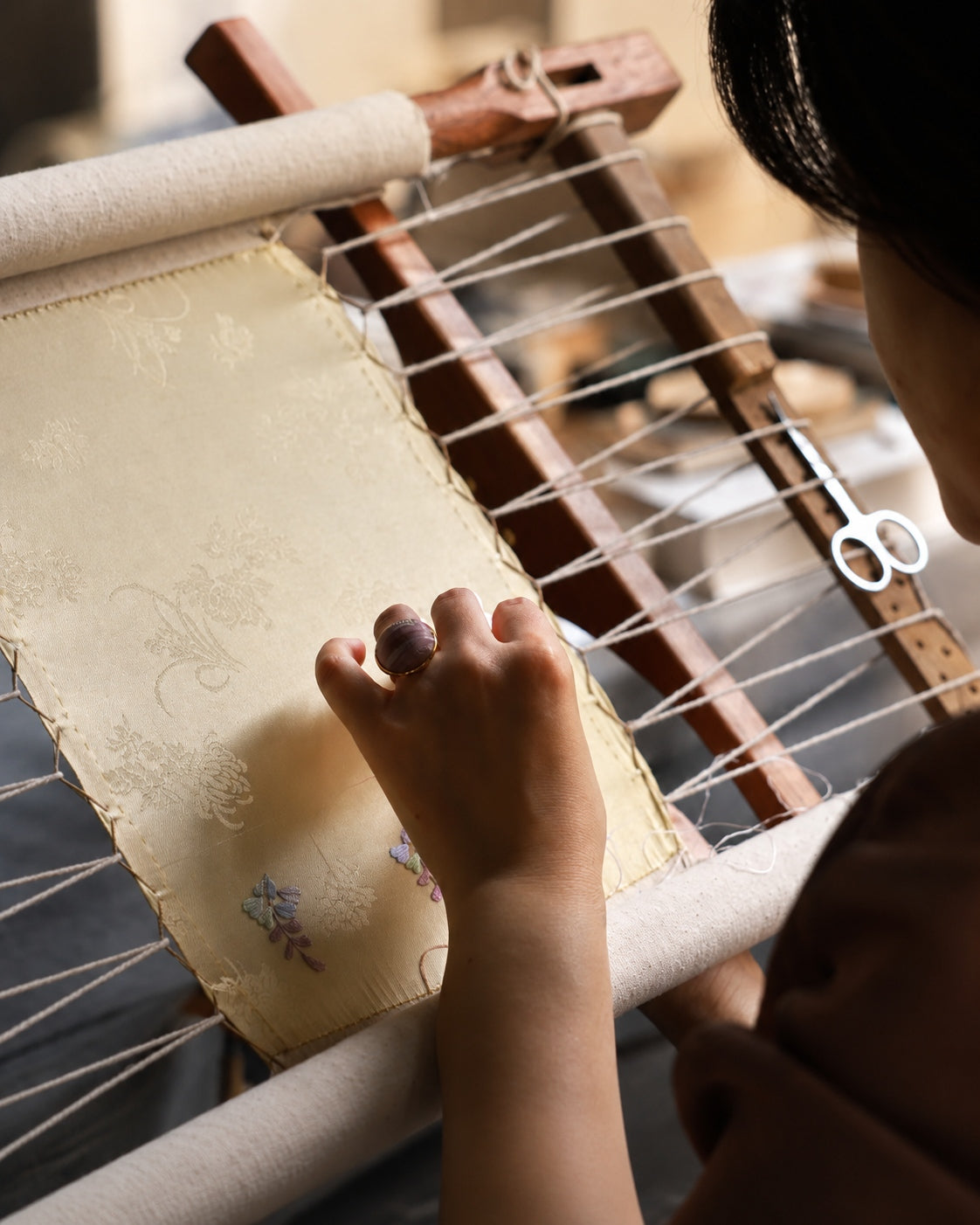 Handworking brocade and embroidery on a frame, expressing textile craftsmanship and heritage artistry for Jinherit Artisan Heritage.