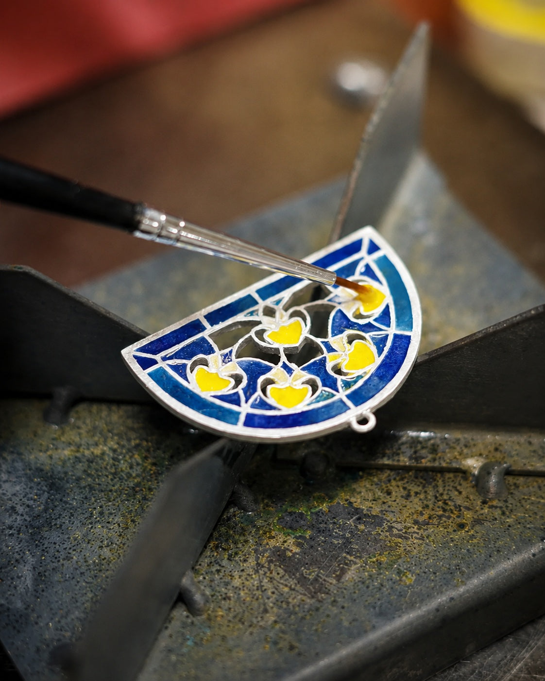 Artisan applying enamel color to a delicate metal pendant, highlighting traditional enamel craftsmanship for Jinherit Artisan Heritage.