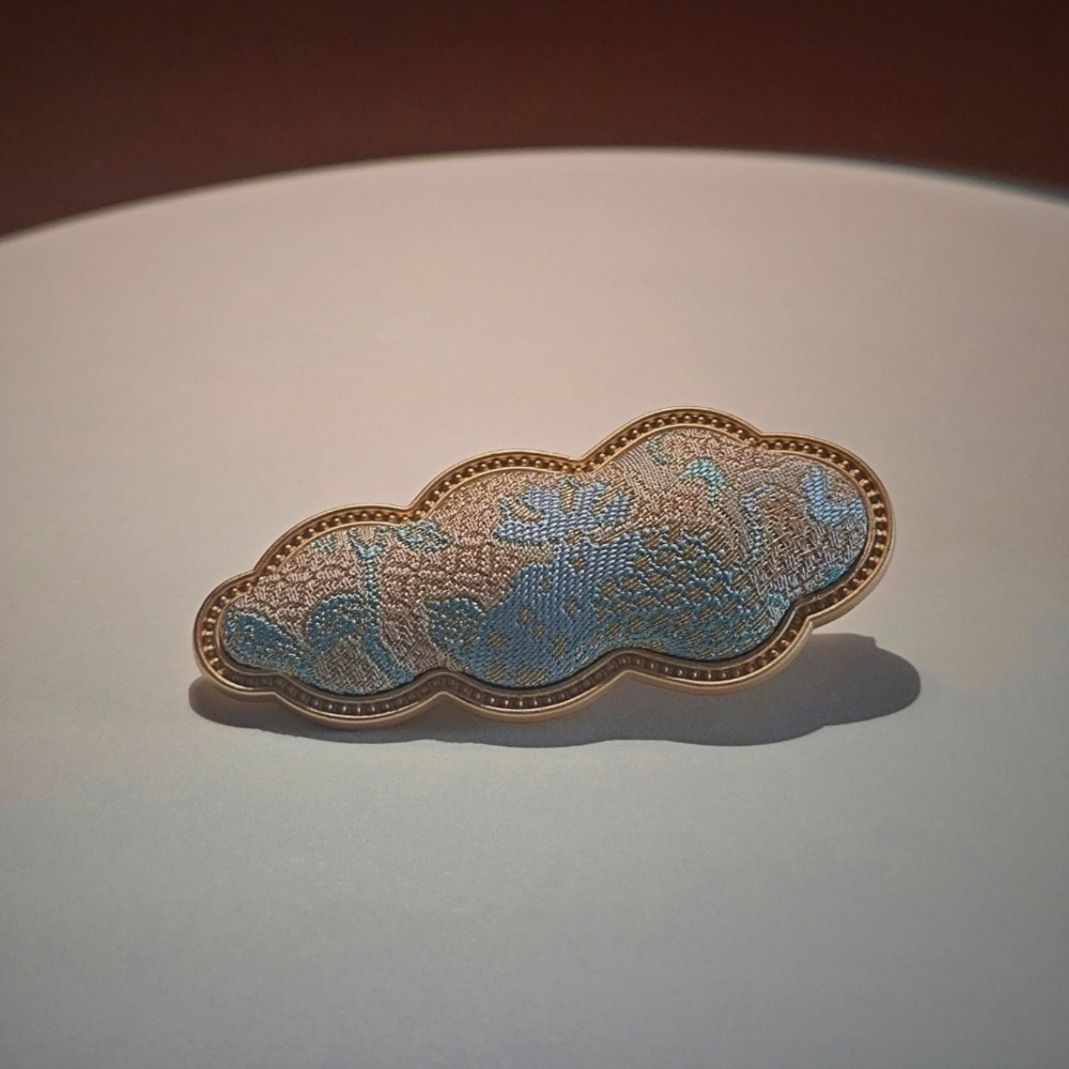 Jinherit Auspicious Cloud Song Brocade silk hair clip in Azure Gold, showing vivid blue and gold brocade texture with an auspicious cloud-inspired silhouette.
