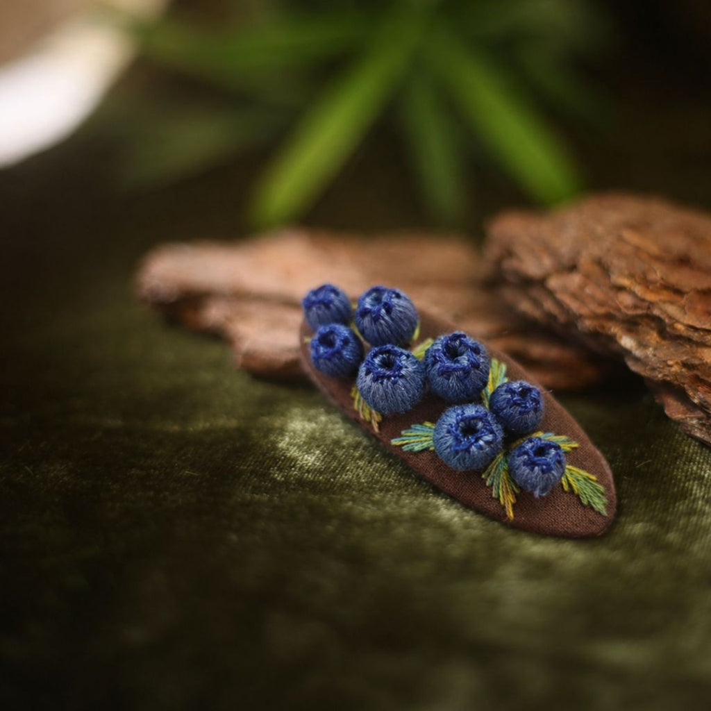 Jinherit Berry Bloom 3D embroidered blueberry Snap Clip displayed in a woodland-style setting, featuring hand-stitched raised berries, green leaves, and a slim snap clip base.
