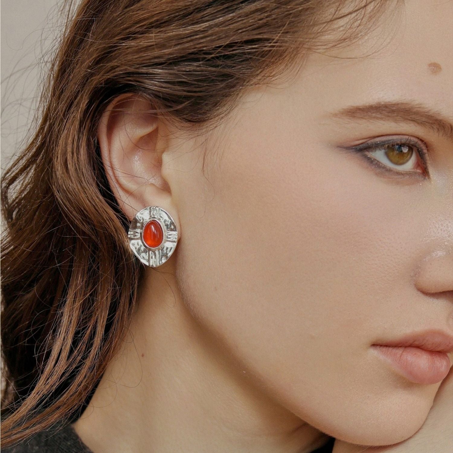 Jinherit Brave Heart red agate and vintage-silver stud earrings worn by a model, showing the bold red stone focal point, hammered silver-tone frame, and refined statement styling.