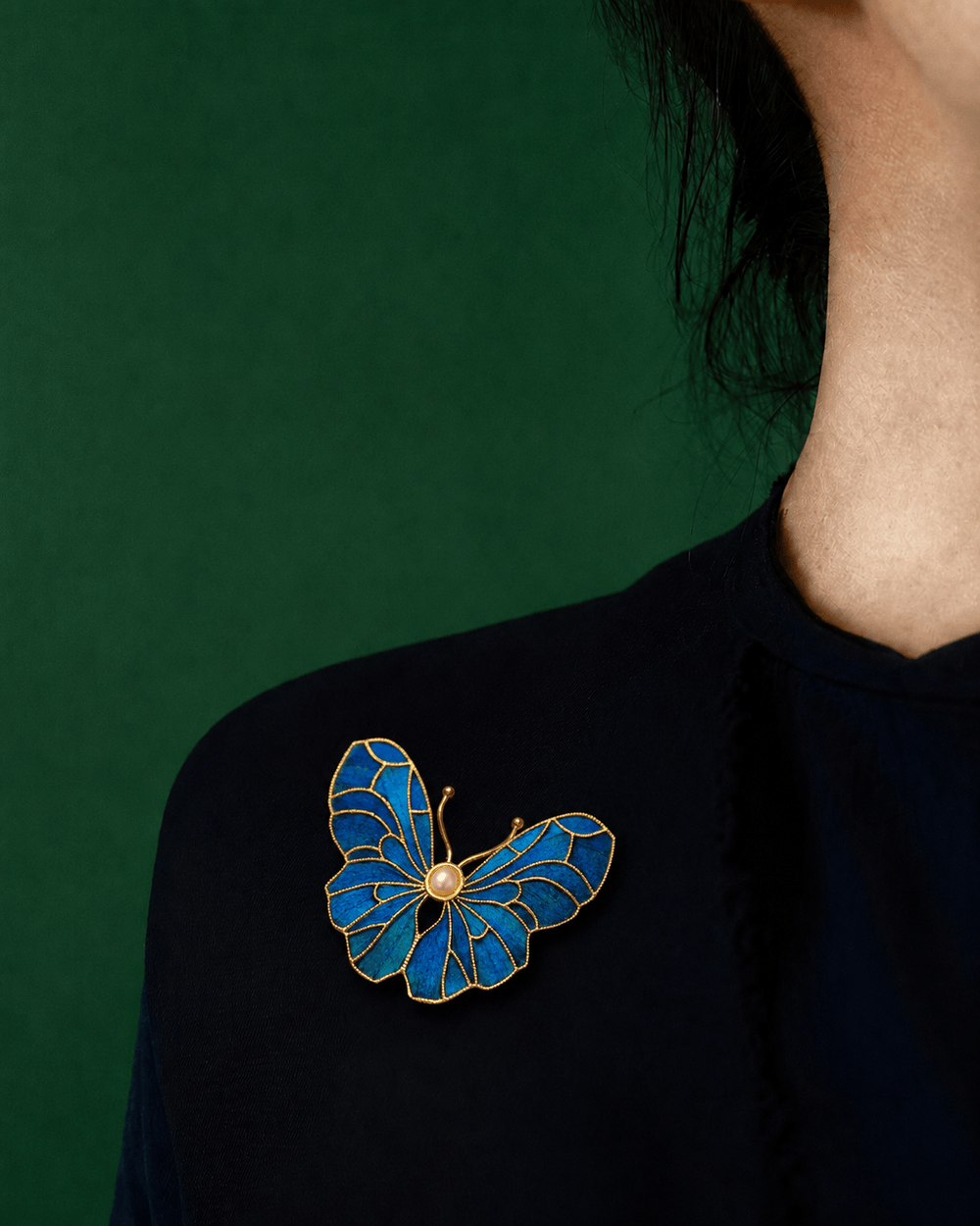 Dian Cui inspired blue butterfly brooch with gold outline and pearl detail on black fabric.