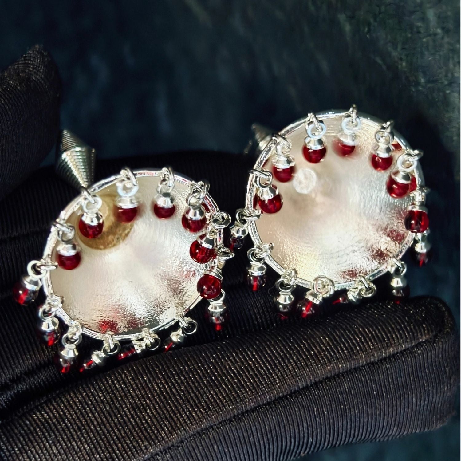Jinherit Crimson Echo garnet bell drop earrings front detail, showing natural garnet bead fringe, sculptural bell-shaped metalwork, and rhythmic silver-tone lines.