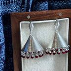 Jinherit Crimson Echo garnet bell drop earrings displayed in a wooden jewelry box, featuring sculptural silver-tone bell forms, spiral texture, and natural garnet fringe.