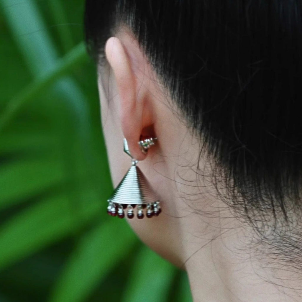 Jinherit Crimson Echo garnet bell drop earrings worn by a model, showing the sculptural drop shape, subtle garnet movement, and heritage-inspired statement styling.