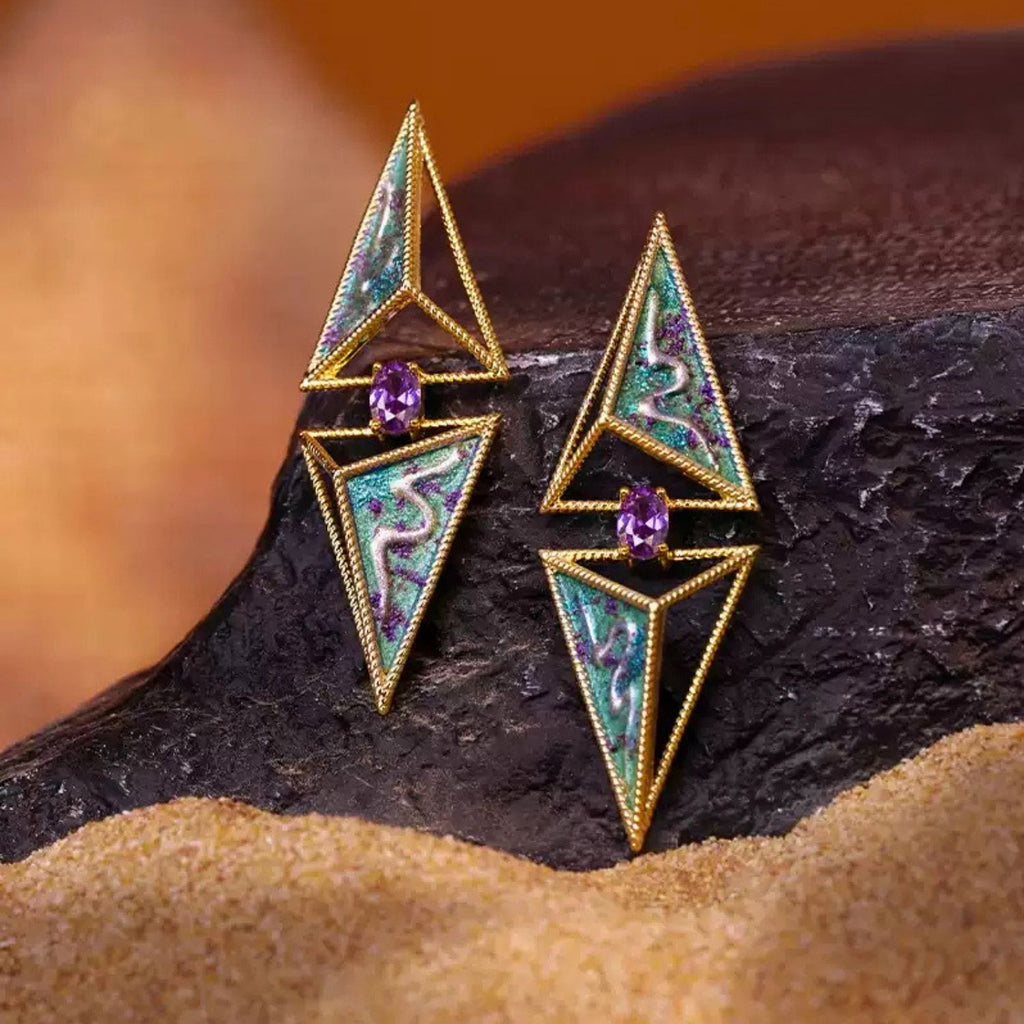 Jinherit Eye of the Desert hand-painted geometric stud earrings styled on a desert-inspired surface, highlighting the sculptural triangular silhouette, painted detail, and artistic gold-plated finish.