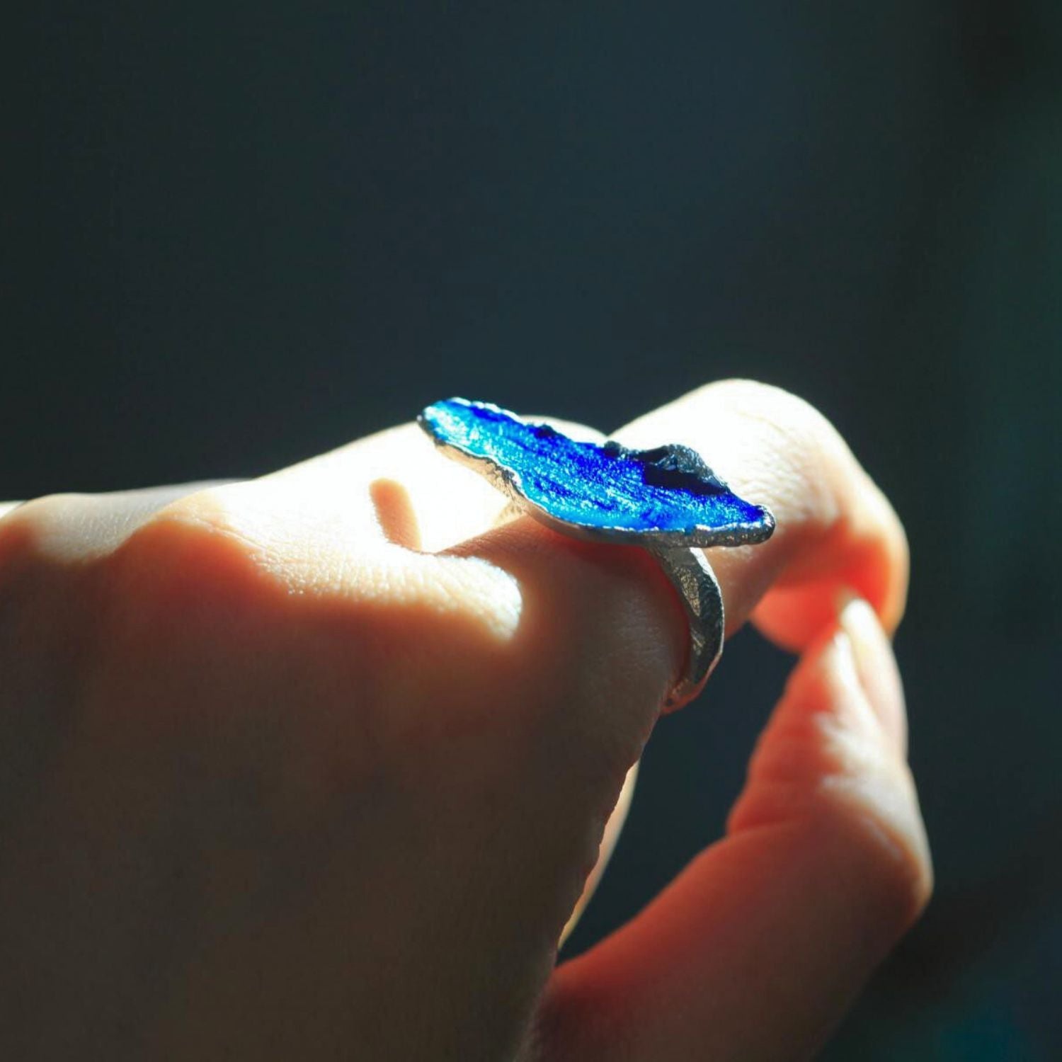 Jinherit Into the Blue blue enamel open ring shown in hand, capturing the luminous enamel glow, irregular silver outline, and nature-inspired wearable art character.