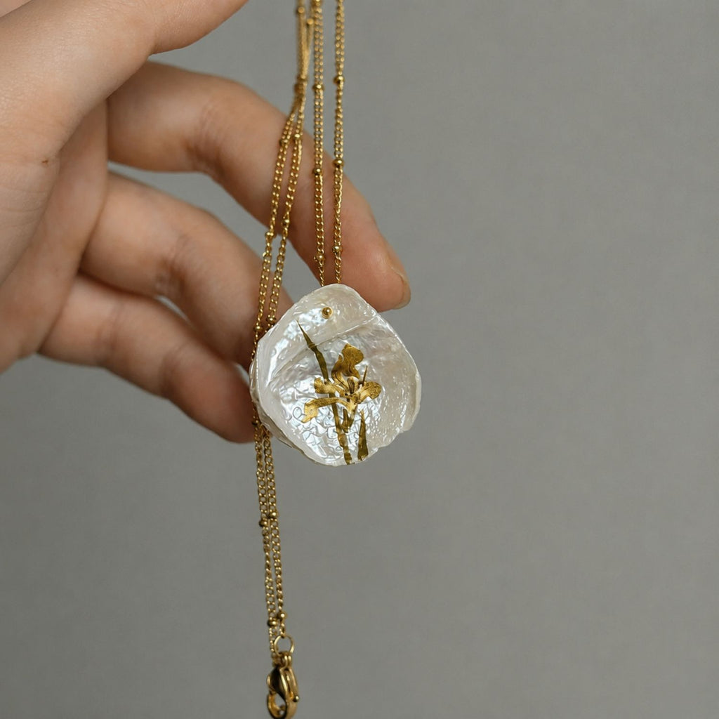 Jinherit Iris on Pearl hand-painted Chinese lacquer freshwater pearl necklace, shown in hand with an organic petal pearl, golden iris brushwork, and a delicate gold-tone chain.