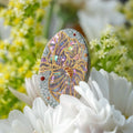 Jinherit Iris Reverie lacquer and mother-of-pearl inlay ring displayed among white flowers, featuring an iris motif, eggshell mosaic, gold accents, and an adjustable sterling silver band.