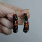 Jinherit Iris Thicket hand-painted Chinese lacquer hoops shown in hand, highlighting the black and red lacquer variants, curved C-hoop silhouette, and delicate iris flower brushwork.