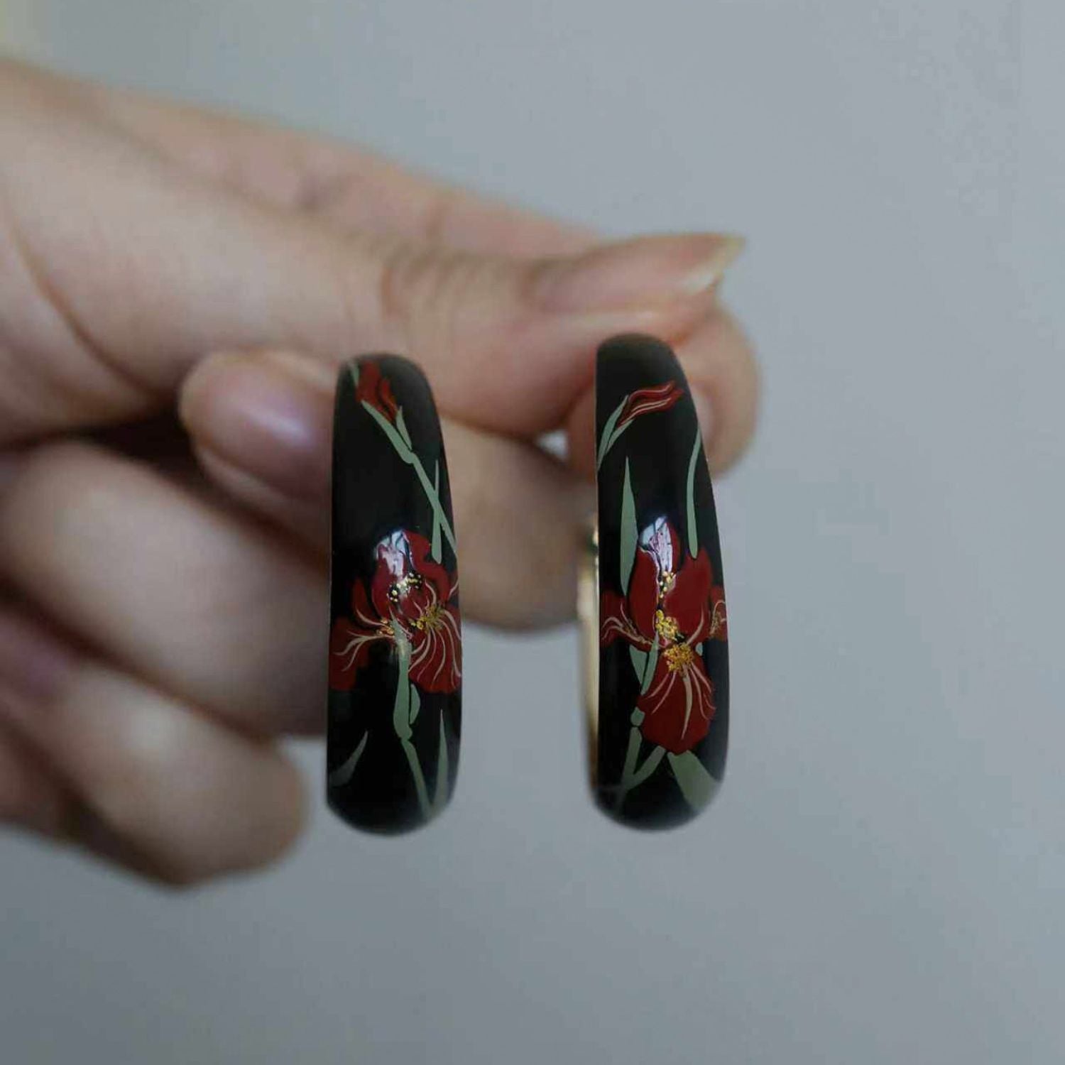 Jinherit Iris Thicket hand-painted Chinese lacquer hoops shown in hand, highlighting the black and red lacquer variants, curved C-hoop silhouette, and delicate iris flower brushwork.
