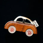 Jinherit Joyride wooden rose quartz car brooch pin, featuring a solid wood car body, rose quartz-toned wheel accents, zircon sparkle, and polished copper detail on a dark background.