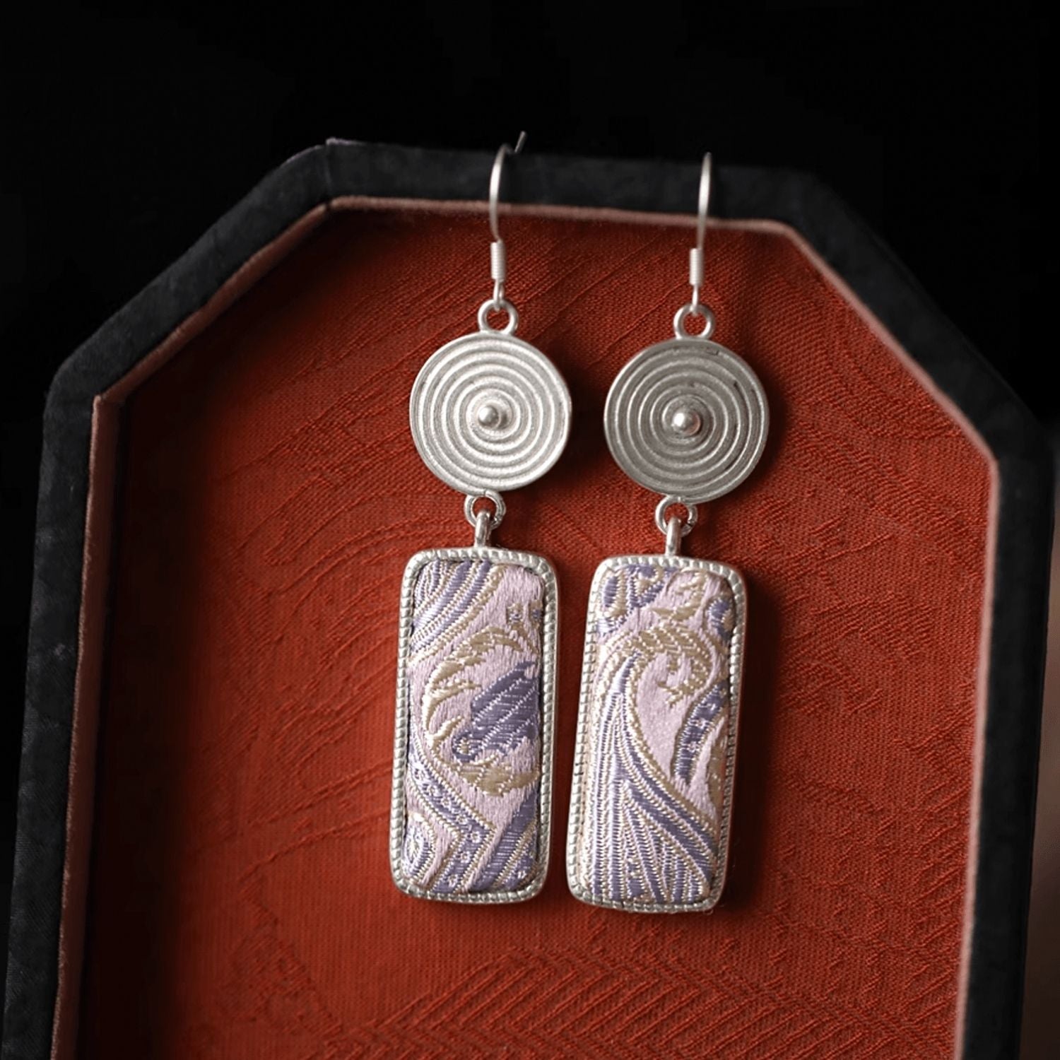 Jinherit Lilac Loom Song Brocade dangle earrings styled on a red tray, highlighting Chinese heritage textile craft, woven shimmer, and refined hook earring design.