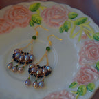 Jinherit Lustrous Tide iridescent pearl tassel drop earrings displayed on a floral plate, featuring freshwater pearl clusters, gold-tone chains, black spinel accents, and soft antique-inspired shimmer.