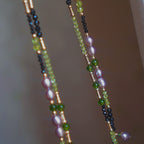 Close detail of Jinherit Lustrous Tide pearl tassel wrap necklace, highlighting metallic-lustre freshwater pearls, black spinel contrast, green peridot accents, and fine hand-beaded texture.