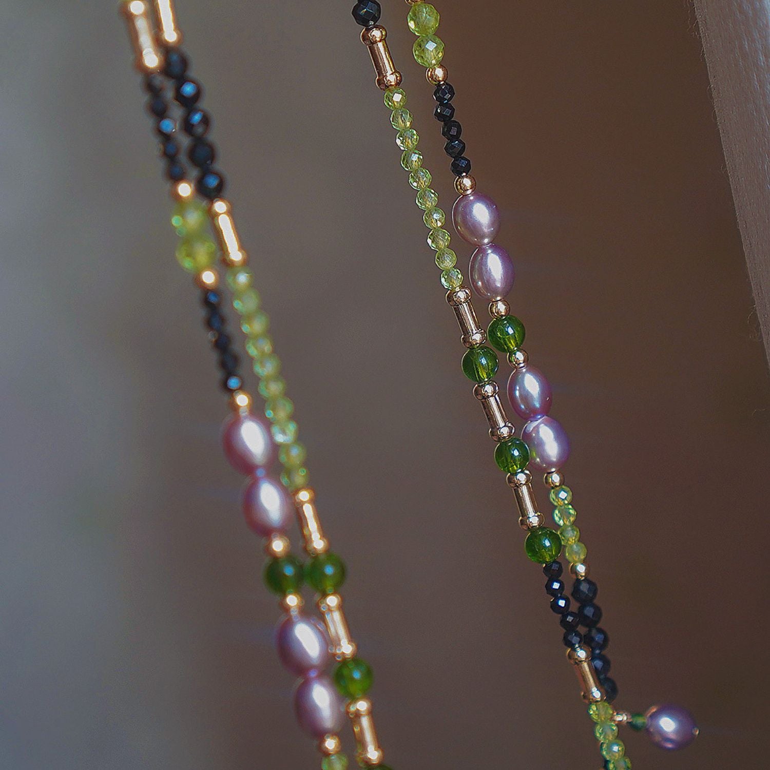 Close detail of Jinherit Lustrous Tide pearl tassel wrap necklace, highlighting metallic-lustre freshwater pearls, black spinel contrast, green peridot accents, and fine hand-beaded texture.