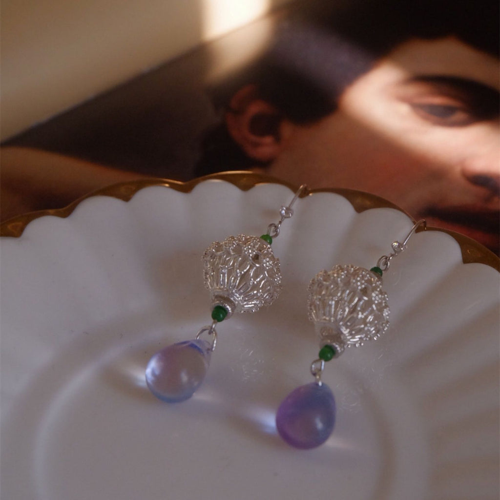 Jinherit Moonlit Lantern silver openwork drop earrings displayed on a shell tray, featuring S925 sterling silver filigree, green jade beads, and purple-blue glass teardrops.