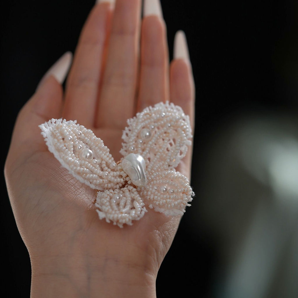Jinherit Pearl Flutter beaded butterfly hair clip shown on hand, highlighting its 3D butterfly shape, delicate seed bead texture, and statement hair accessory scale.
