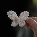 Jinherit Pearl Flutter hand-beaded butterfly hair clip shown in hand, featuring seed bead wings, a selected natural pearl centre, and a sculptural butterfly silhouette.