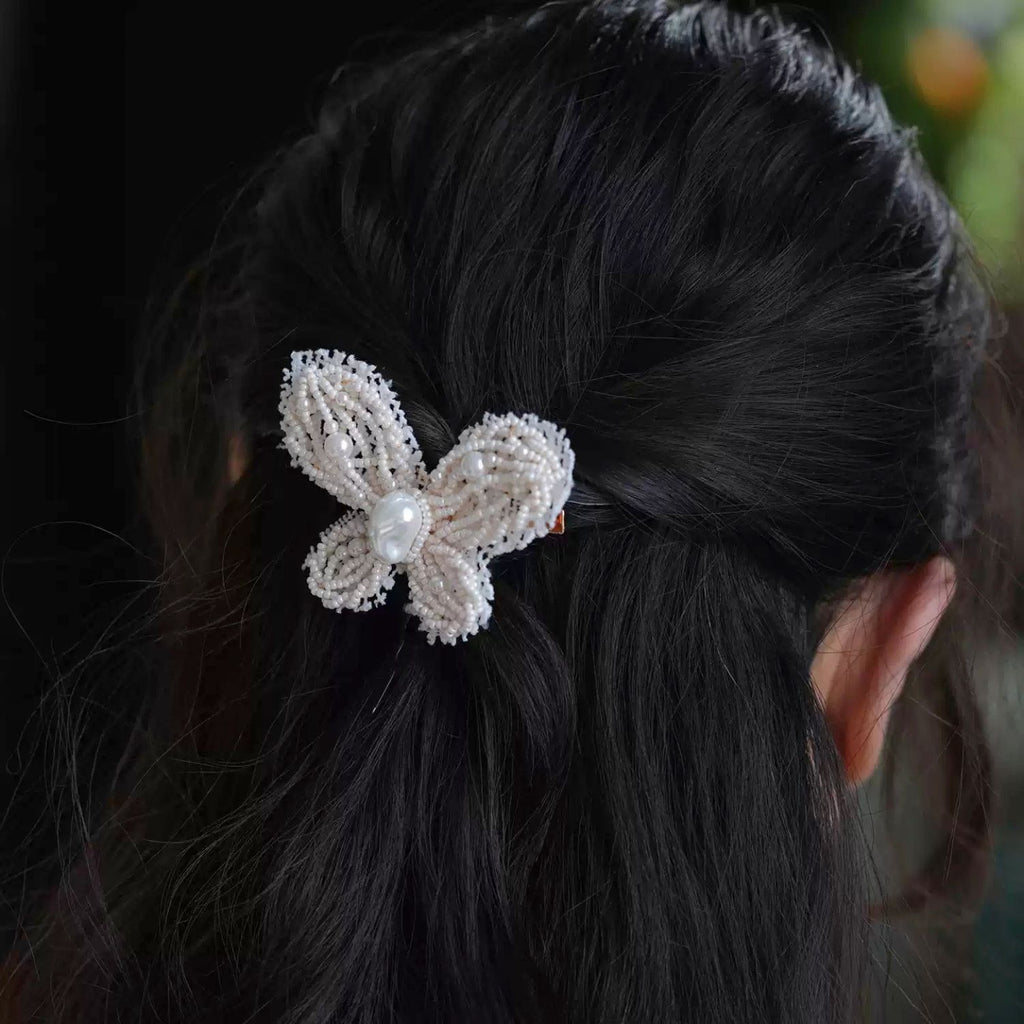 Jinherit Pearl Flutter hand-beaded butterfly hair clip worn in hair, showing the pearl-centred butterfly design, romantic bridal mood, and polished back-hair styling.