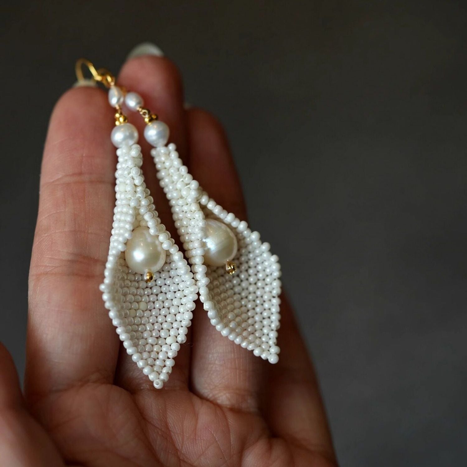 Jinherit Pure Calla beaded calla pearl drop earrings shown in hand, highlighting the airy floral form, hand-beaded white seed bead texture, and natural freshwater pearl accent.