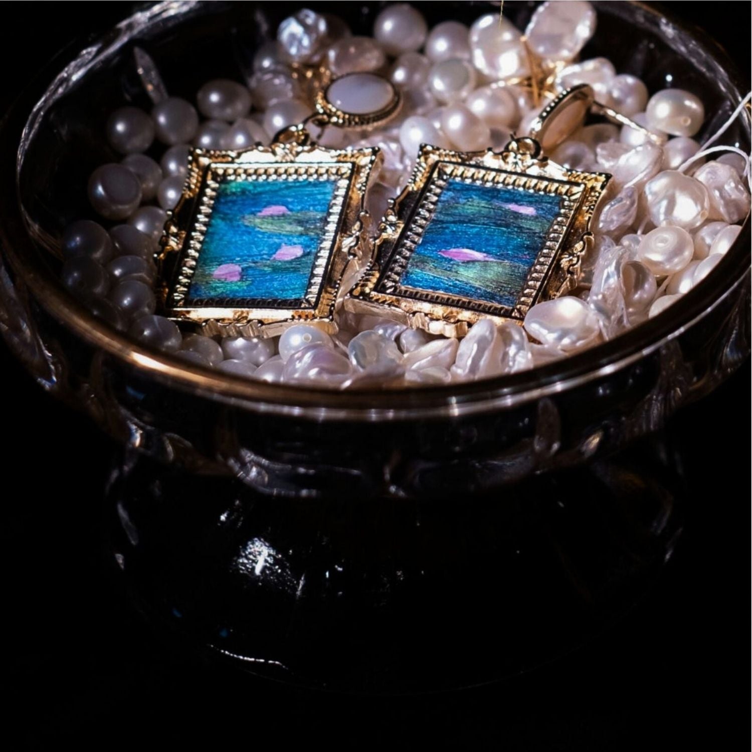 Jinherit Water Lily Dream feather inlay drop earrings displayed in a jewelry box, showing the Dian Cui-inspired feather surface, 14K gold-plated frame, and mother-of-pearl detail.