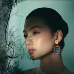 Jinherit Water Lily Dream feather inlay drop earrings worn by a model, highlighting the framed water lily motif, iridescent blue-green feather color, and artistic statement styling.