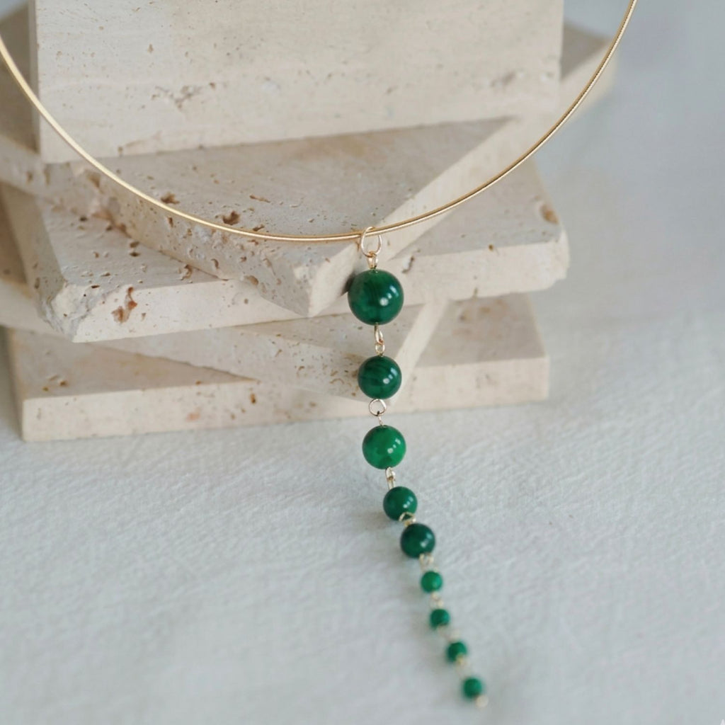 Jinherit Zen Line emerald-green Y-drop lariat necklace flat lay, showcasing a gold-plated collar arc and a long vertical drop of graduated emerald-green beads in a modern minimalist design.
