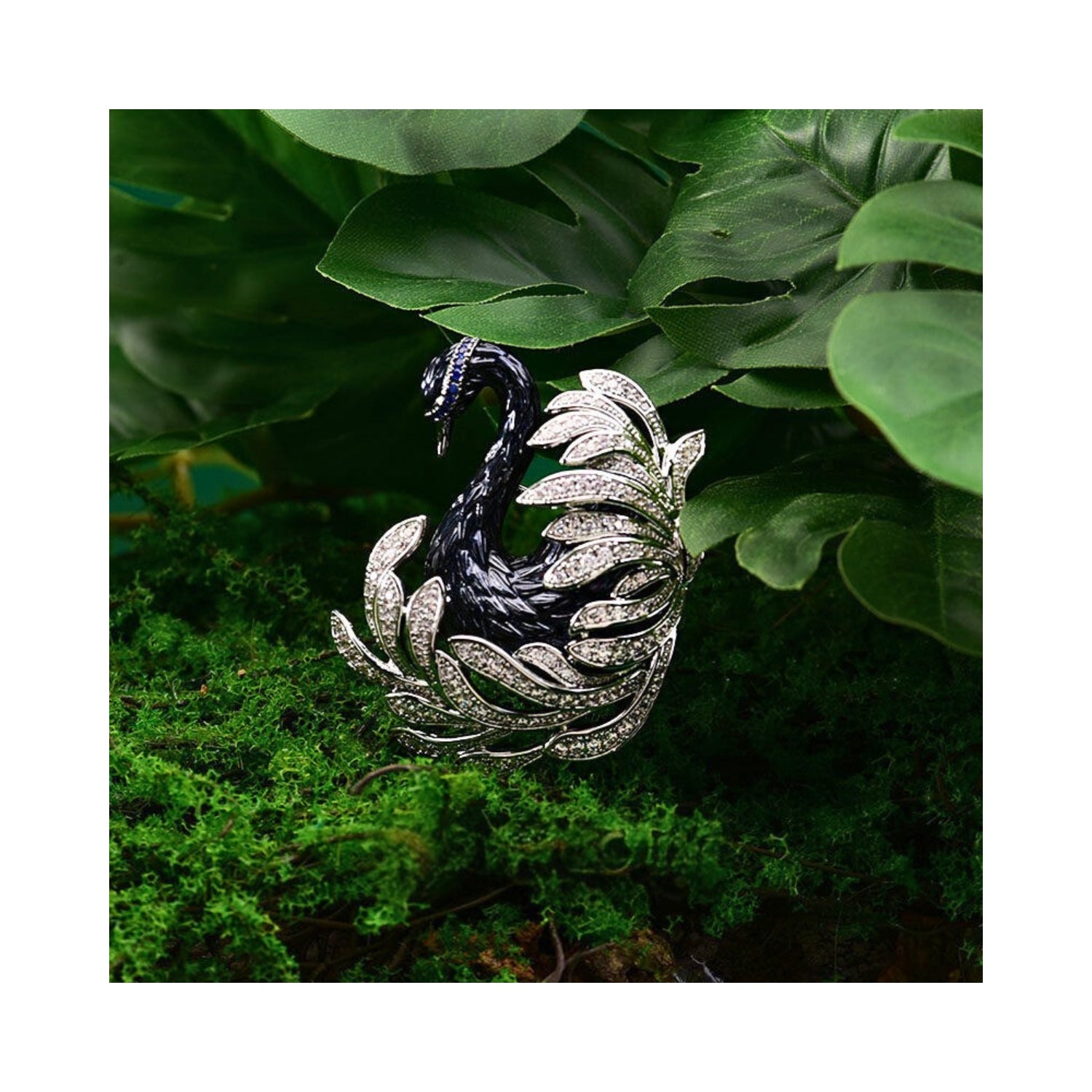 Jinherit Midnight Grace black swan crystal brooch shown in a moss garden setting, highlighting sculptural swan form, pavé zircon feather lines, and Austrian blue crystal accents.