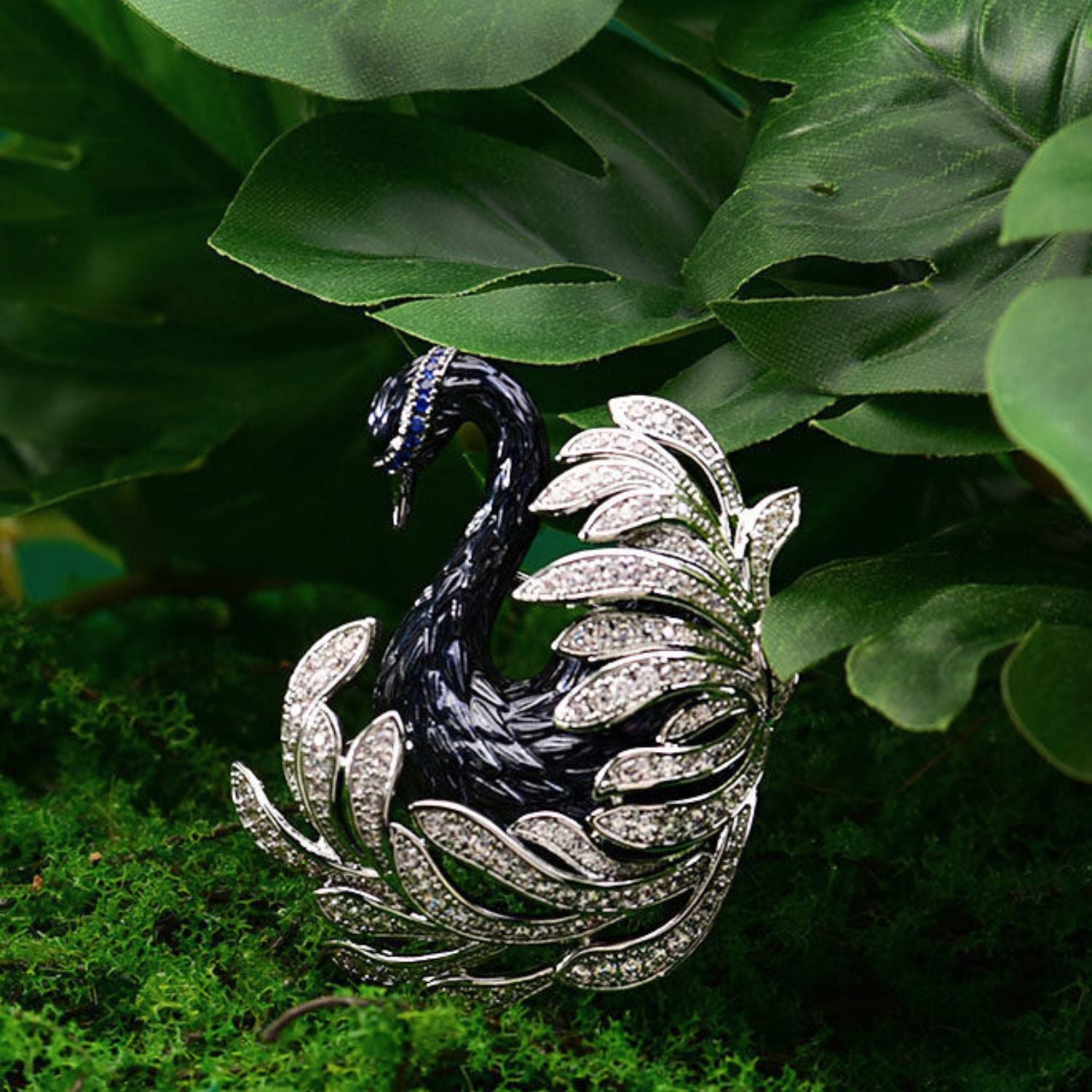 Midnight Grace black swan crystal brooch with silver-tone feather detail and blue crystal accents on green leaves.