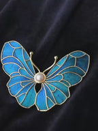 Jinherit Whispering Wings Dian Cui butterfly brooch pin shown in a wearing detail video, highlighting peacock feather inlay, blue structural iridescence, freshwater pearl center, and gold-tone linework.