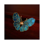 Angled front view of Whispering Wings Dian Cui butterfly brooch on a wooden surface, showing vivid blue iridescence and layered wing shape.