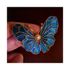 Handheld view of Whispering Wings Dian Cui butterfly brooch showing artisanal scale, feather texture, and luminous blue wing panels.