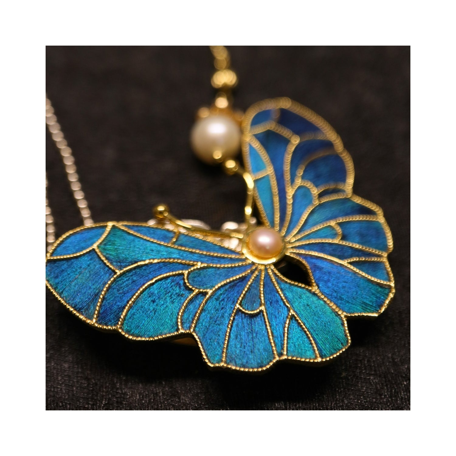 Close-up detail of Whispering Wings Dian Cui butterfly brooch with peacock feather inlay, pearl center, and gold-tone outline.
