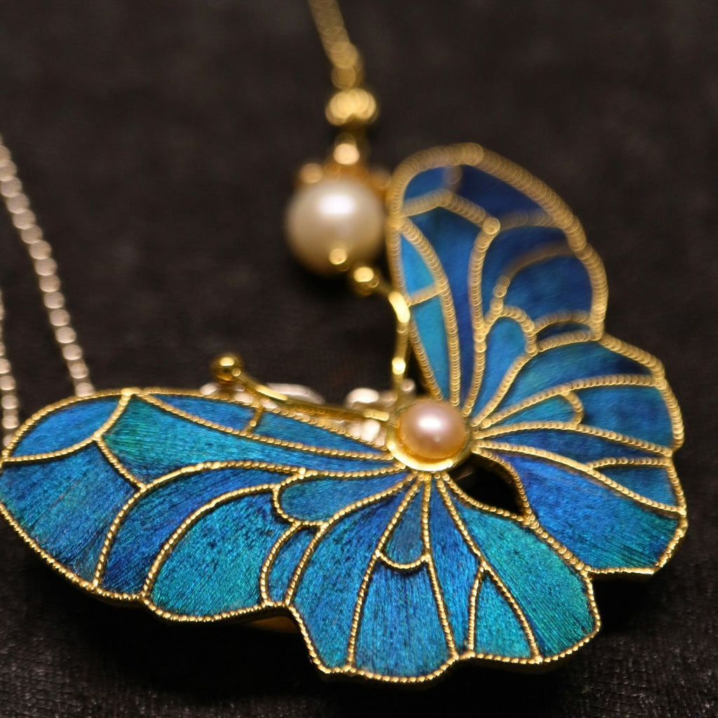 Whispering Wings Dian Cui-inspired butterfly brooch with peacock-feather inlay, gold-toned lines, and freshwater pearl detail.
