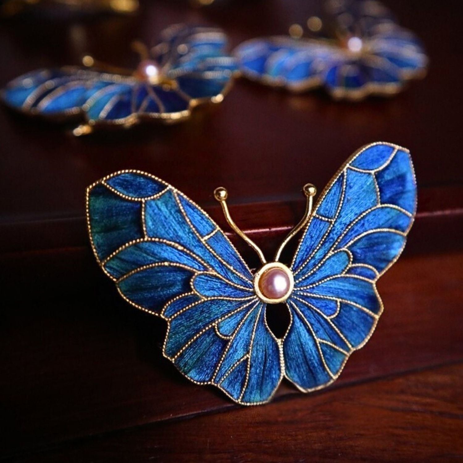 Close-up of peacock-feather butterfly brooch with blue-green iridescence and gold wing structure.
