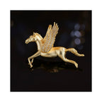 Close-up of Wings of Inspiration Pegasus pavé horse brooch in gold tone on a dark background, highlighting the sculpted flying horse form, crystal-set wing, and polished metallic finish.